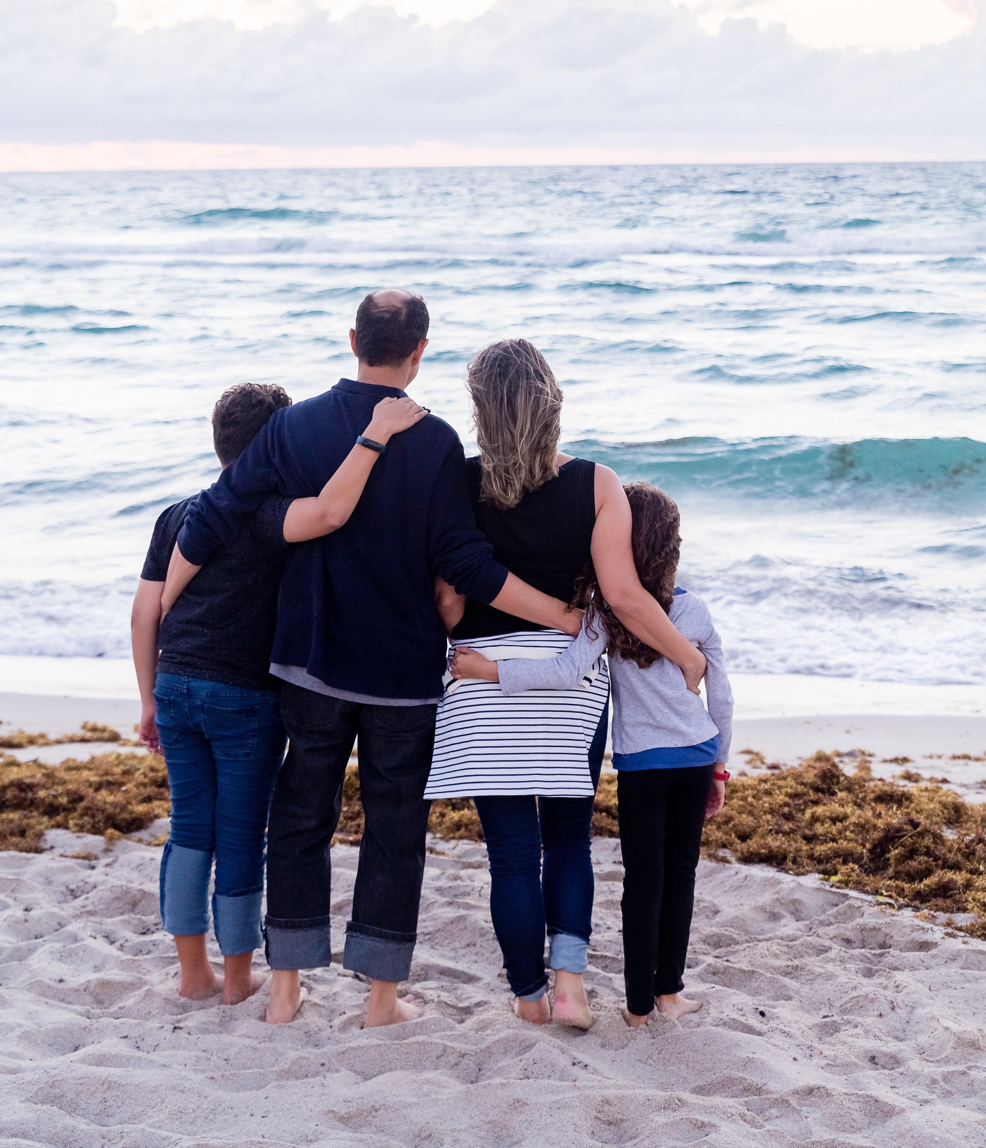 Stock bilde av ein familie som står på stranden og held rundt kvarandre.