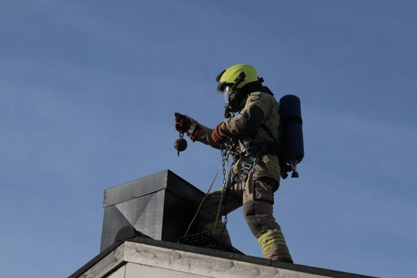 Bildet viser ein brannmann på eit tak, ved ei pipe. - Klikk for stort bilete
